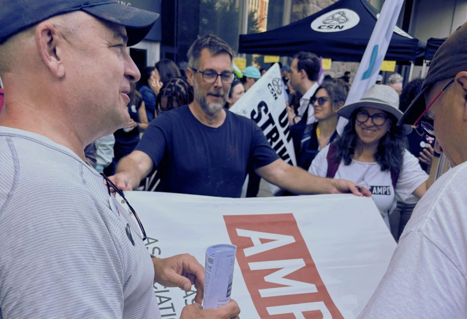 Groupe de manifestant·es lors d'un rassemblement syndical, portant des bannières de l'AMPD et de la CSN, discutant ensemble avec enthousiasme.