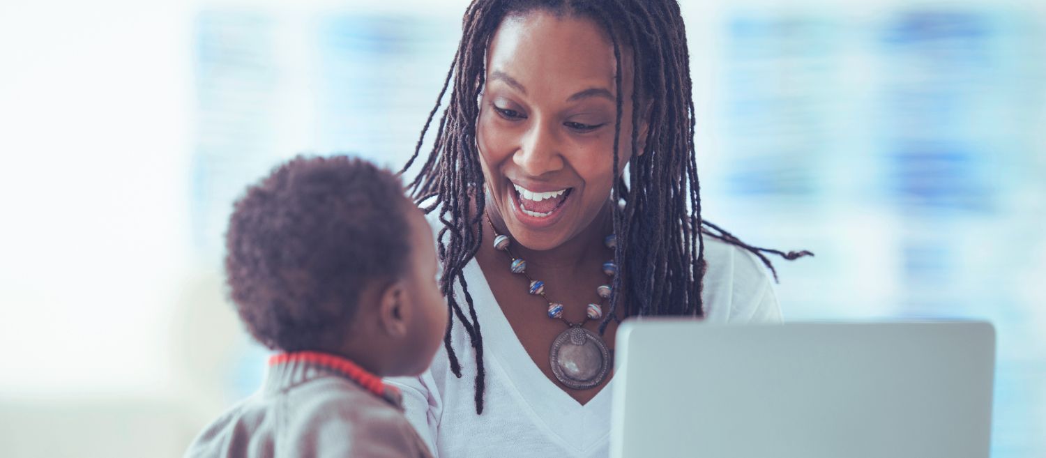 Mère souriante travaillant sur un ordinateur tout en interagissant avec son enfant, illustrant la conciliation entre travail et vie familiale.