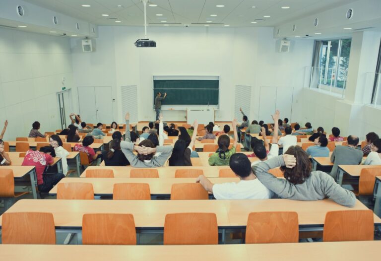 Salle de cours universitaire où des étudiant·es lèvent la main, illustrant les enjeux du projet de loi 9 sur la laïcité et l’autonomie universitaire.