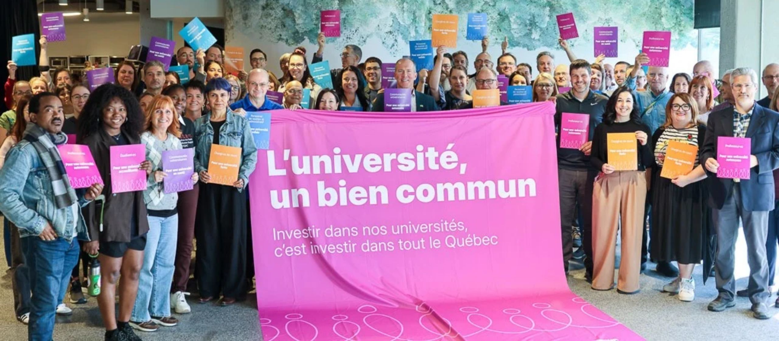 Grand groupe de membres des communautés universitaires derrière une bannière « L’université, un bien commun ».