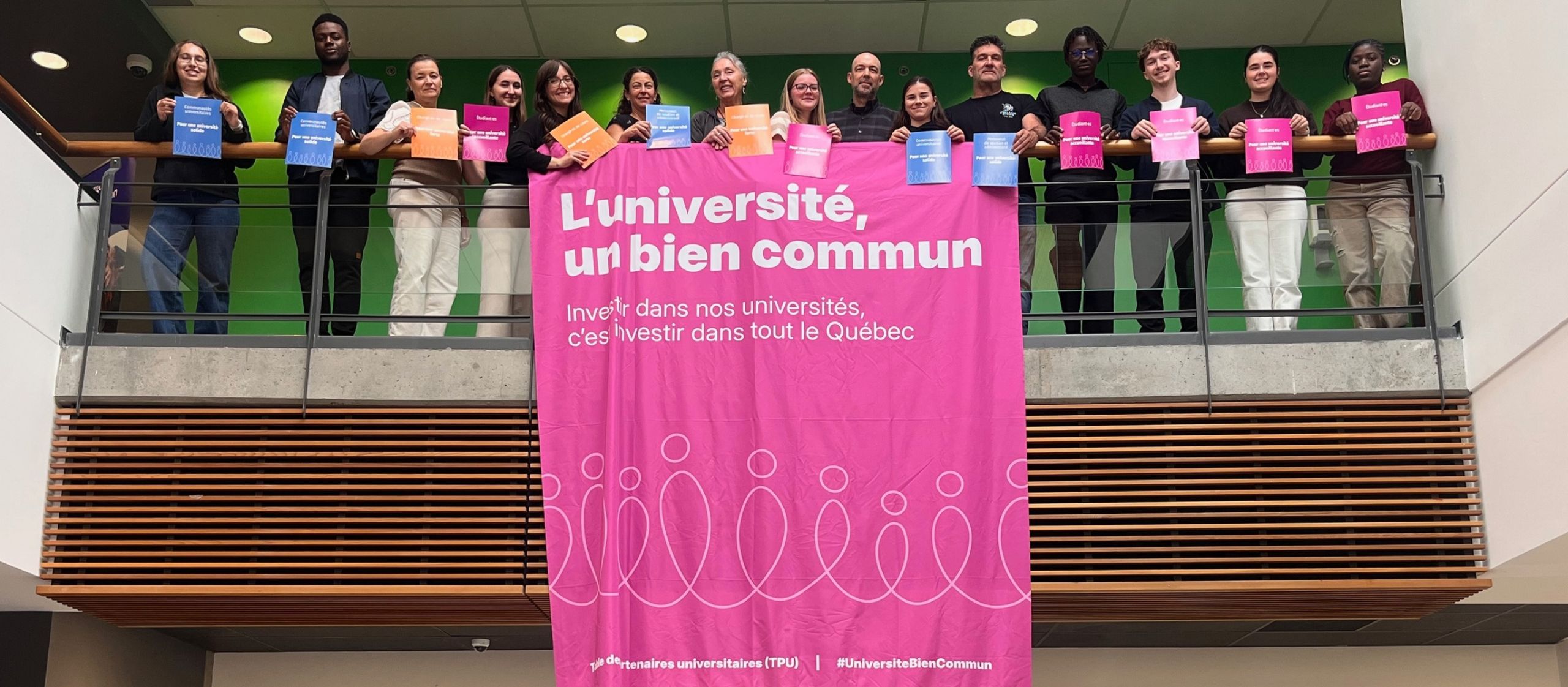 Des membres de la communauté universitaire posent derrière une grande bannière « L’université, un bien commun » en tenant des affiches colorées.